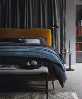 Letto con testiera arancione e biancheria da letto blu con panca posizionata ai piedi del letto.