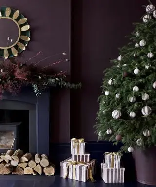 Uma sala de estar roxa com lareira azul-marinho decorada com uma guirlanda de abeto, uma árvore de natal cheia de bugigangas ao lado