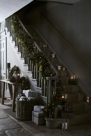 Entrada de Natal com paredes escuras, guirlanda de escada, luminárias nas escadas, mesa de console com guirlanda e velas, cesta de.gif