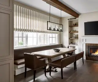 Sala de jantar com janela atrás e lareira à direita com TV em cima