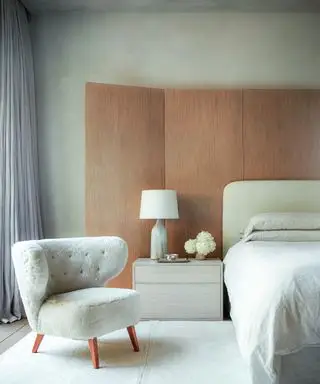 quarto branco com cadeira de pele de carneiro branca dos anos 1940, cama branca, biombo de madeira, tapete e abajur brancos e gavetas de cabeceira