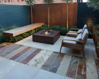 Se muestra cómo colocar un patio en un patio moderno y elegante con varios colores de adoquines y una fogata de bronce.