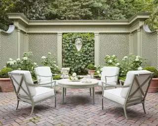 En have med udendørs opholdsområde, grønne og hvide møbler og salviegrønt espalier