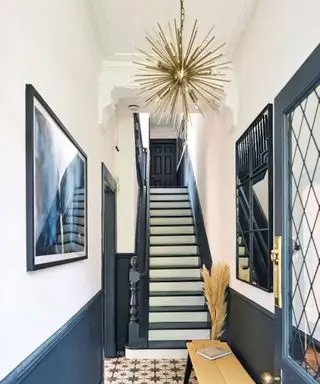 Pasillo pintado de azul y blanco, elementos de madera pintados de azul oscuro, escaleras pintadas, lámpara colgante de metal, banco con pasto de pampa decorativo