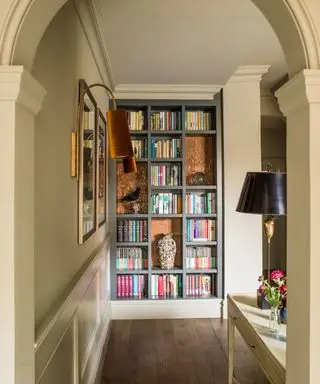 Úzká chodba s šedou natřenou knihovnou a architektonickým obloukem.