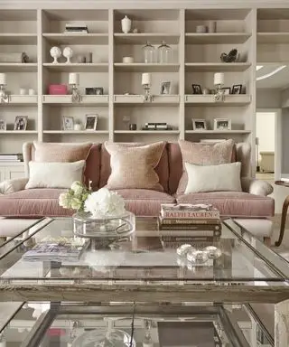 En rosa sofa foran store hvite vegghyller og et salongbord