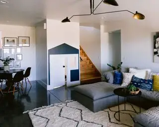 Kjellerombygging med seksjonssofa, sidebord og teppe, spisebord og stoler, lekehus for barn og hvite vegger og mørkt gulv