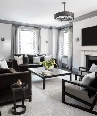 Schwarz-graues modernes Wohnzimmer mit grau gestrichener Deckenverkleidung, grauen Vorhängen, zwei schwarzen Sofas, großem quadratischem Couchtisch und schwarzem Sessel, abgerundeter Metallpendelleuchte und passendem Beistelltisch, Sitzbereich rund um den Kamin