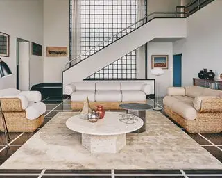 Conjunto de sofá e poltrona em sala ampla, tapete creme grande, mesa de centro redonda de mármore, paleta neutra