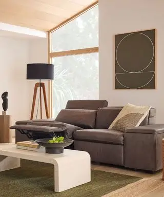 Sofá de couro reclinável em uma sala de estar moderna e iluminada, luminária de chão grande, obras de arte na parede, mesa de centro de mármore