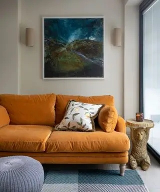 Sofá laranja na sala creme, tapete azul e obras de arte, pufe azul