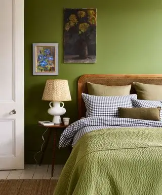 Quarto verde com cabeceira de vime, manta verde, mesa de cabeceira com abajur