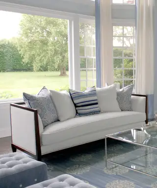 Biała sofa z niebieskimi poduszkami i dużym oknem widokowym.