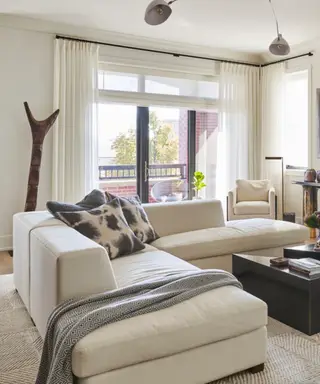 Neutralny salon z dużymi oknami i białą sofą