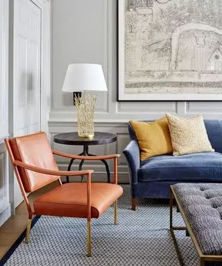 Salón con paredes revestidas de color gris pálido. una silla de cuero marrón y un sofá azul y una mesa circular.