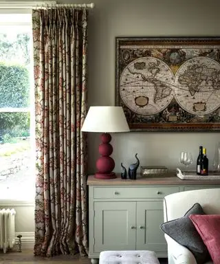 Biblioteca en el vestíbulo con suelos de madera, armario de cáscara de huevo, taburete tapizado en color beige y ventana con cortinas con motivos florales
