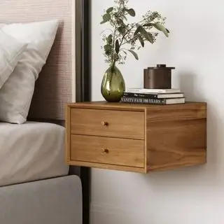 Un conjunto de cajones flotantes de madera junto a una cama, con un jarrón y una pequeña pila de libros encima.