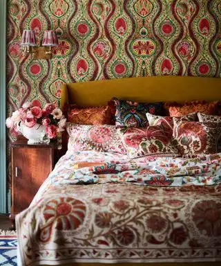 Papier peint maximaliste derrière le lit dans la chambre avec de nombreux imprimés floraux campagnards