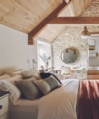 Quarto com piso de madeira, tapete de rattan, cama de casal abaixo do teto abobadado.