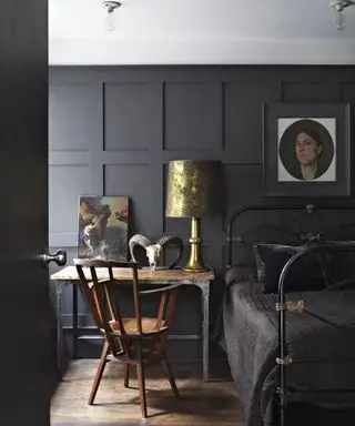 Una estructura de cama de metal negro en una habitación de color azul intenso combina con un escritorio y una silla de madera.