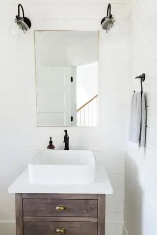 חדר אמבטיה צבוע לבן עם קירות shiplap לבנים אבזור ואביזרים שחורים ומראת פליז