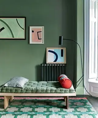 Grøn gang med malede grønne vægge, daybed med træramme og grønne puder, abstrakt kunst på vægge i blåt og pink, grønt mønstret tæppe, sort gulvlampe ved siden af daybed