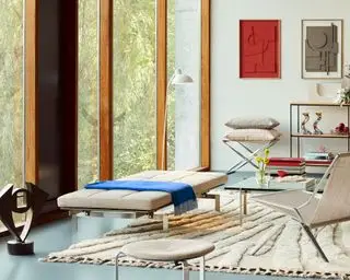 Fritz Hansen PK kollektion i moderne stue, daybed, lænestol, glas sofabord, gulv til loft glasvinduer, hylder og kunst i baggrunden