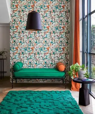 Værelse med grønne vægge, futon med grøn pude, grønt tæppe på sort gulv og indrammede moderne kunstbilleder.