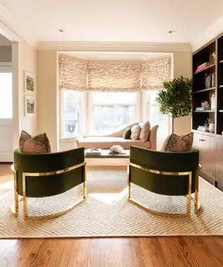 Moderne stue med to lænestole ud mod en karnap, daybed under vinduet, trægulv med stort tæppe, indbygget reol