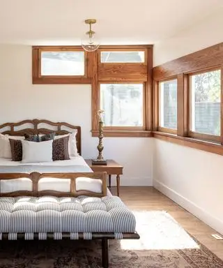 Soveværelse med unikke firkantede vinduer med trærammer, dobbeltseng med træramme, daybed med stribet polstring ved fodenden af sengen, trægulv