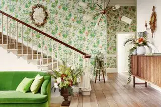 sala com sofá verde, corredor, escadas, piso de madeira, papel de parede floral verde