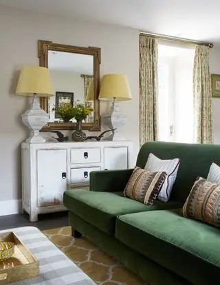 sala com sofá verde, aparadores com duas luminárias de mesa combinando e espelho