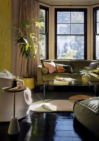 sala de estar com sofá verde, mesa de centro de vidro, piso pintado de preto, plantas, janela saliente, poltronas, mesa lateral, luminária de chão, detalhes em preto
