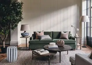 sala terrosa com sofá verde, ninho de mesinhas laterais, tapete texturizado, shiplap, plantas, acessórios em formato orgânico, piso de madeira