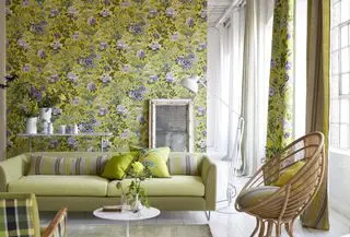sala de estar com papel de parede floral amarelo, sofá verde limão, piso pintado de branco, luminária de chão branca, cadeira de vime, acessórios brancos