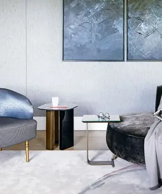 Nowoczesny salon z dwoma eleganckimi stolikami bocznymi, dużą grafiką na ścianie i niebieskim aksamitnym fotelem