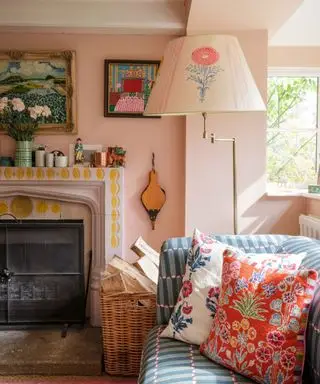 Sala de estar colorida e rosa com almofadas estampadas, lareira de azulejos, obras de arte nas paredes, luminária de chão com abajur decorado floral