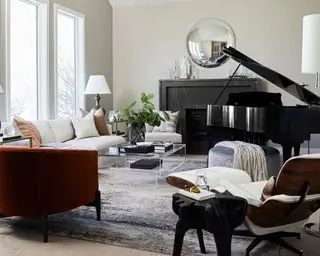 Lys, moderne stue med sort klaver, sort marmor pejs, rundt spejl, hvid læder vitra eames lænestol, gråt tæppe, sofa, glas sofabord