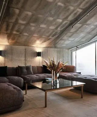 Stor stue i industriel stil med grå hjørnesofa to væglamper, sofabord i træ og sort glas med tørret blomsterarrangement