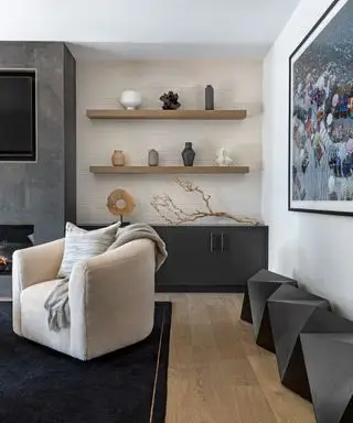 Moderne stue med svævende træhylder dekoreret med ornamenter, sort skænk, sorte geometriske taburetter, creme lænestol, tv, pejs, kunst på væggen