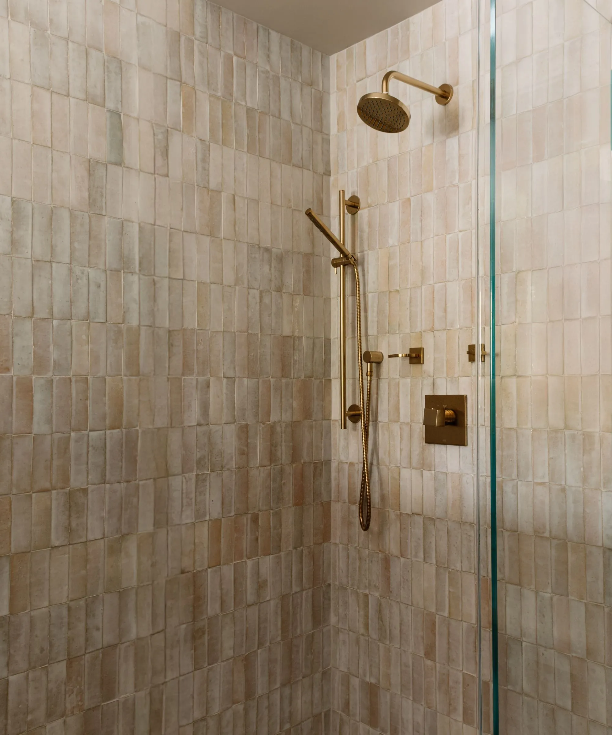 Walk in shower med guldbeslag og beige teksturerede fliser' loading='lazy' title=