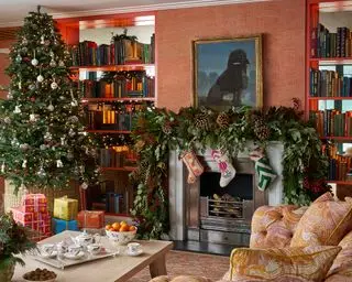 Fargerik stue med peis dekorert med løvverk og strømper, stort juletre med innpakkede gaver