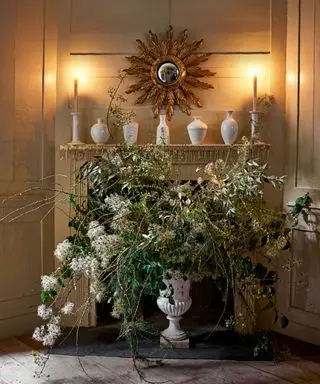 Peis dekorert med stearinlys, keramikk og vase med blomster og løvverk
