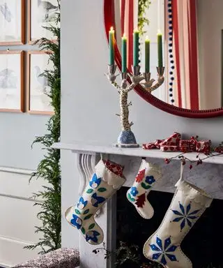Julestrømper hengende fra en peishylle med tente lys i en lysestake foran speilet.