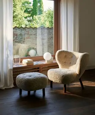 Saueskinn lenestol og matchende fotskammel ved siden av vinduet, lav skjenk dekorert med lampe, bøker og ornamenter, mørkt tregulv, rene gardiner