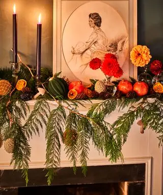 Mantelstykke med innrammet bilde og tente lys, dekorert med blomster, løvverk og tørket frukt