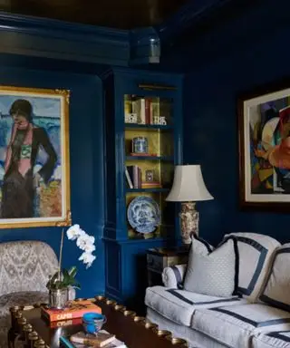 Una sala de estar azul oscuro con un sofá azul y blanco, estanterías y obras de arte.