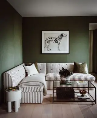 Papel pintado verde, sofá a rayas en forma de L, mesa de centro de cristal