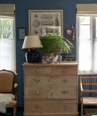 Una habitación azul con una cómoda antigua, dos sillas y obras de arte.