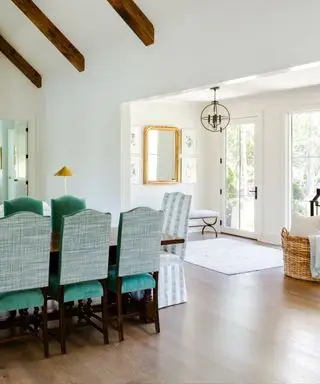 Entrada e sala de jantar brancas com cadeiras de veludo verde.